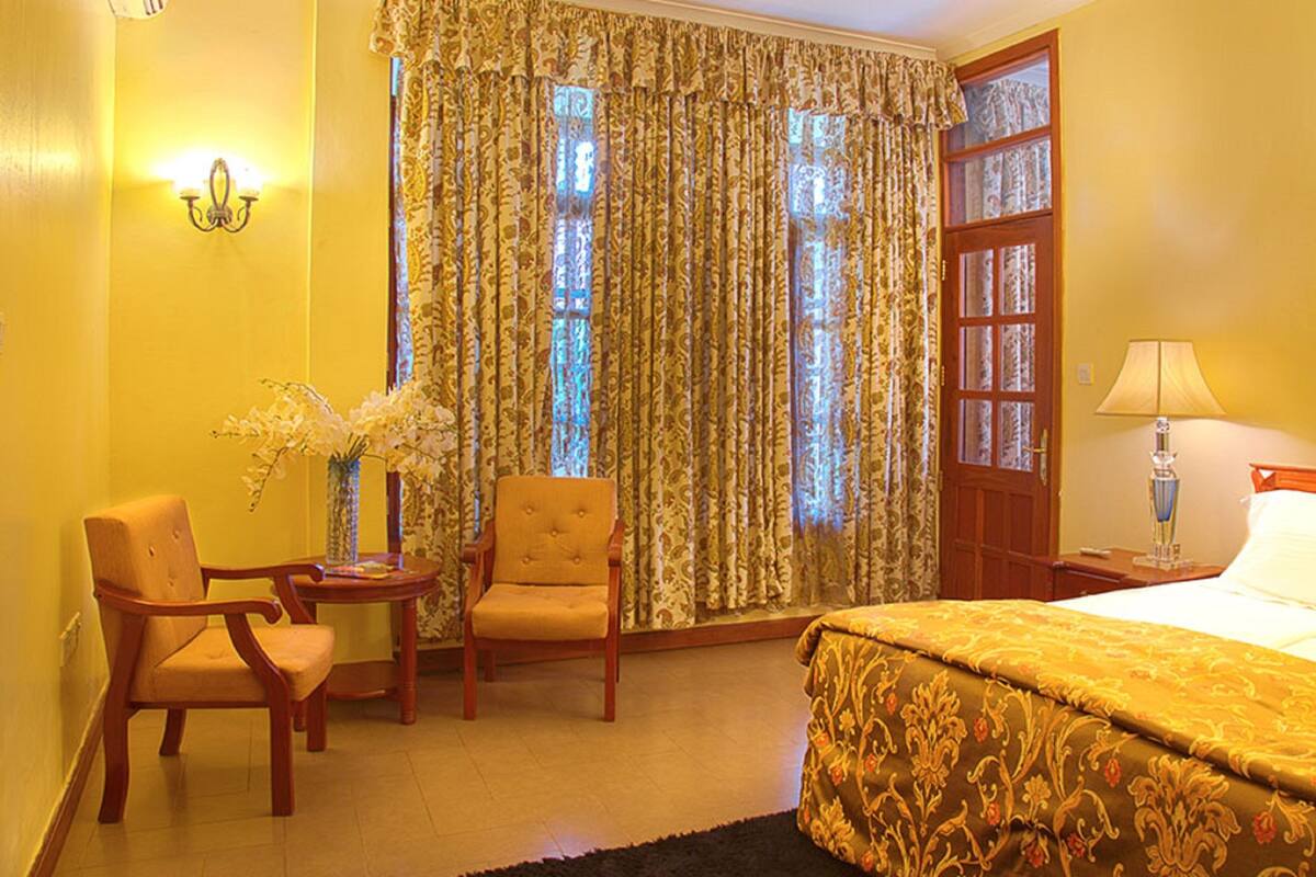 A hotel room with a bed, a chair, a small table, a lamp, and a window with curtains.