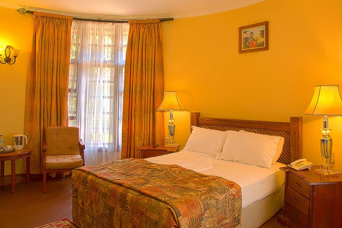 A hotel room with a bed, two bedside lamps, a chair, a bedside table with a phone, and a picture on the wall.