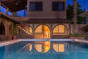 A modern house with a swimming pool, arched windows, and a balcony.