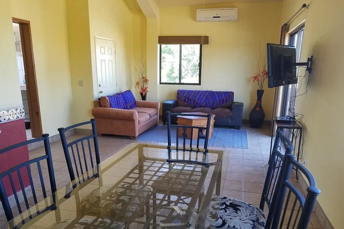 Un salon avec une table à plateau en verre, deux canapés et un téléviseur fixé au mur.