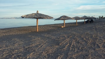 A beach with thatched umbrellas and a car parked on the sand.