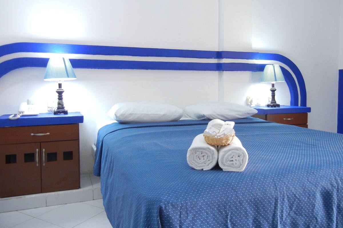 A hotel room with a bed, two nightstands, a lamp on each, a telephone, and a basket of towels.