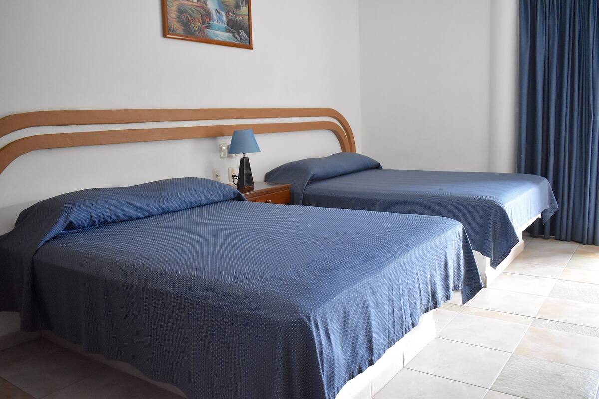 A hotel room with two beds, a nightstand, a lamp, and a painting on the wall.