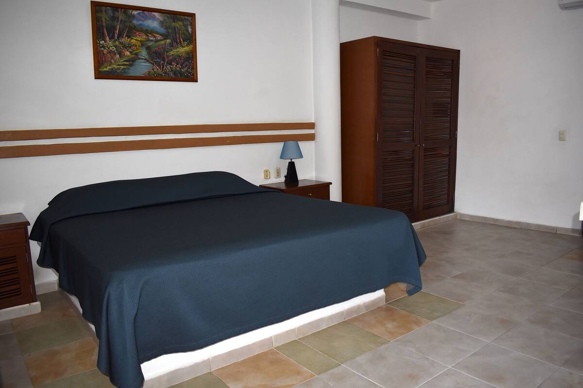 A bedroom with a bed, a nightstand, a lamp, a wardrobe, and a painting on the wall.