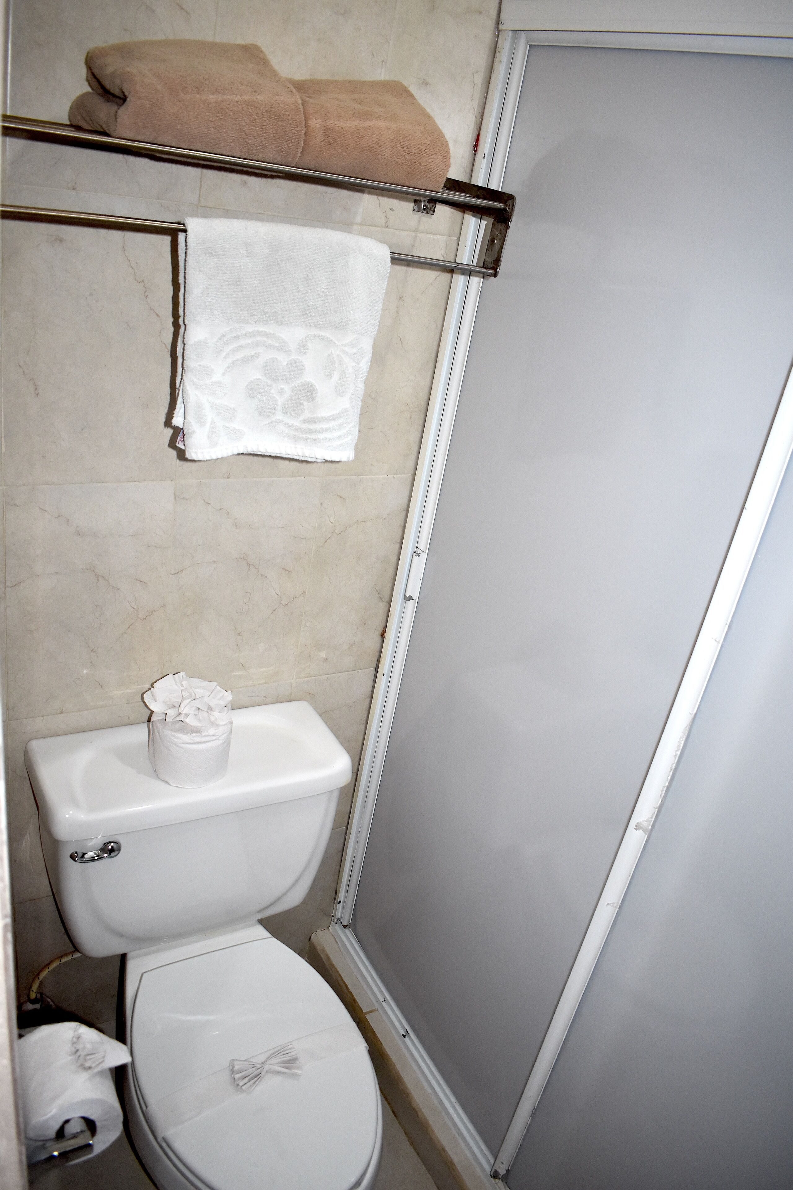A bathroom with a toilet, a towel rack with towels, and a toilet paper holder.