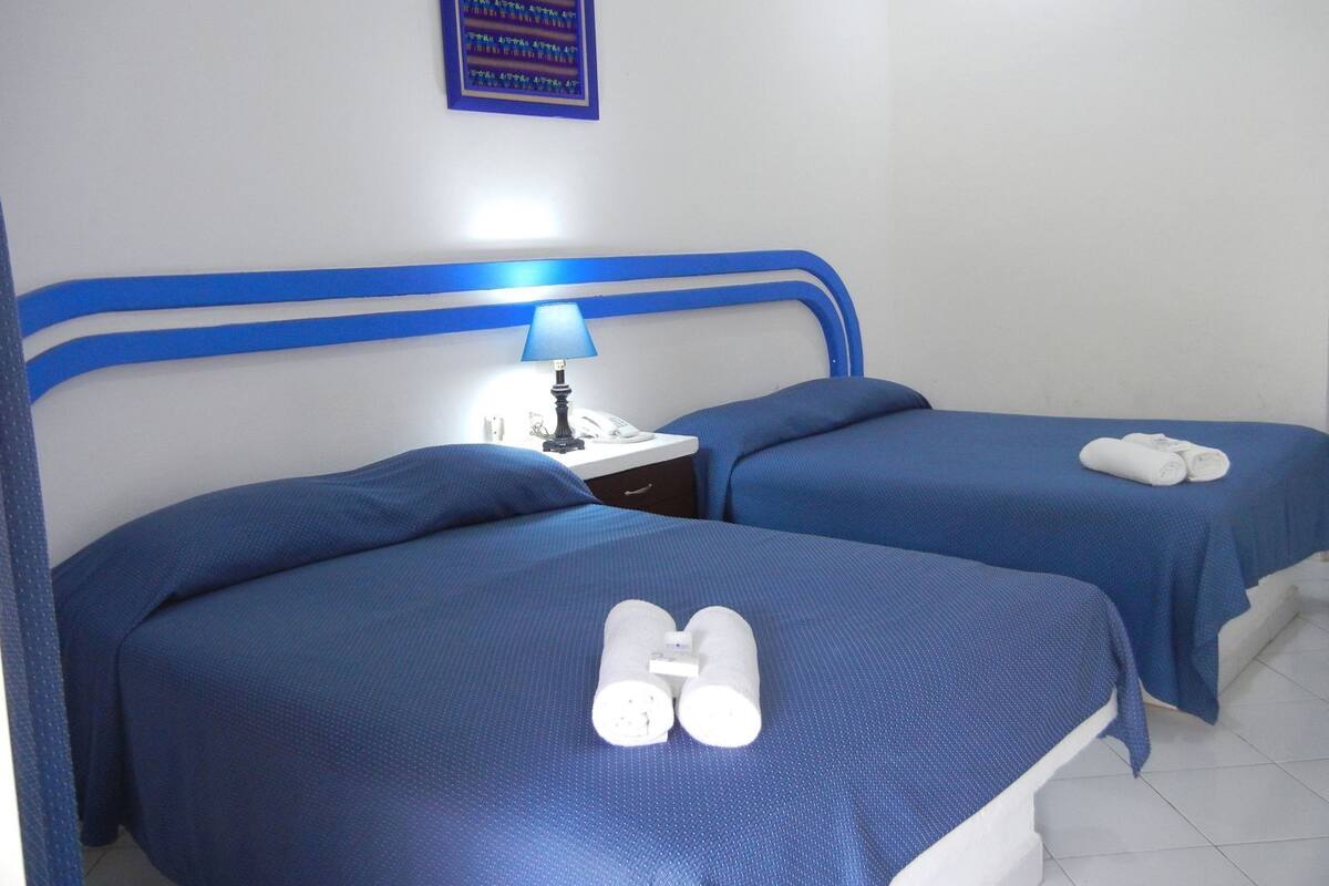 A hotel room with two beds, a nightstand with a lamp, and a wall sign.