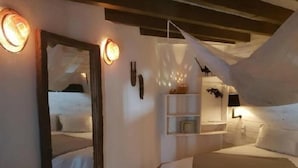 A bedroom with a bed, a mirror, a shelf with decorative items, and a hanging light fixture. - La Ribaudière (Antananarivo)