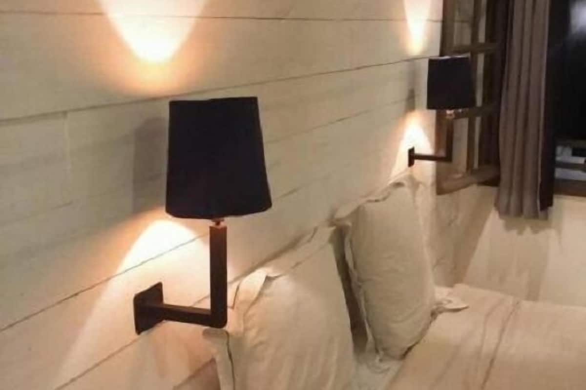 A hotel room with a bed, two wall-mounted lamps, and a window with curtains.