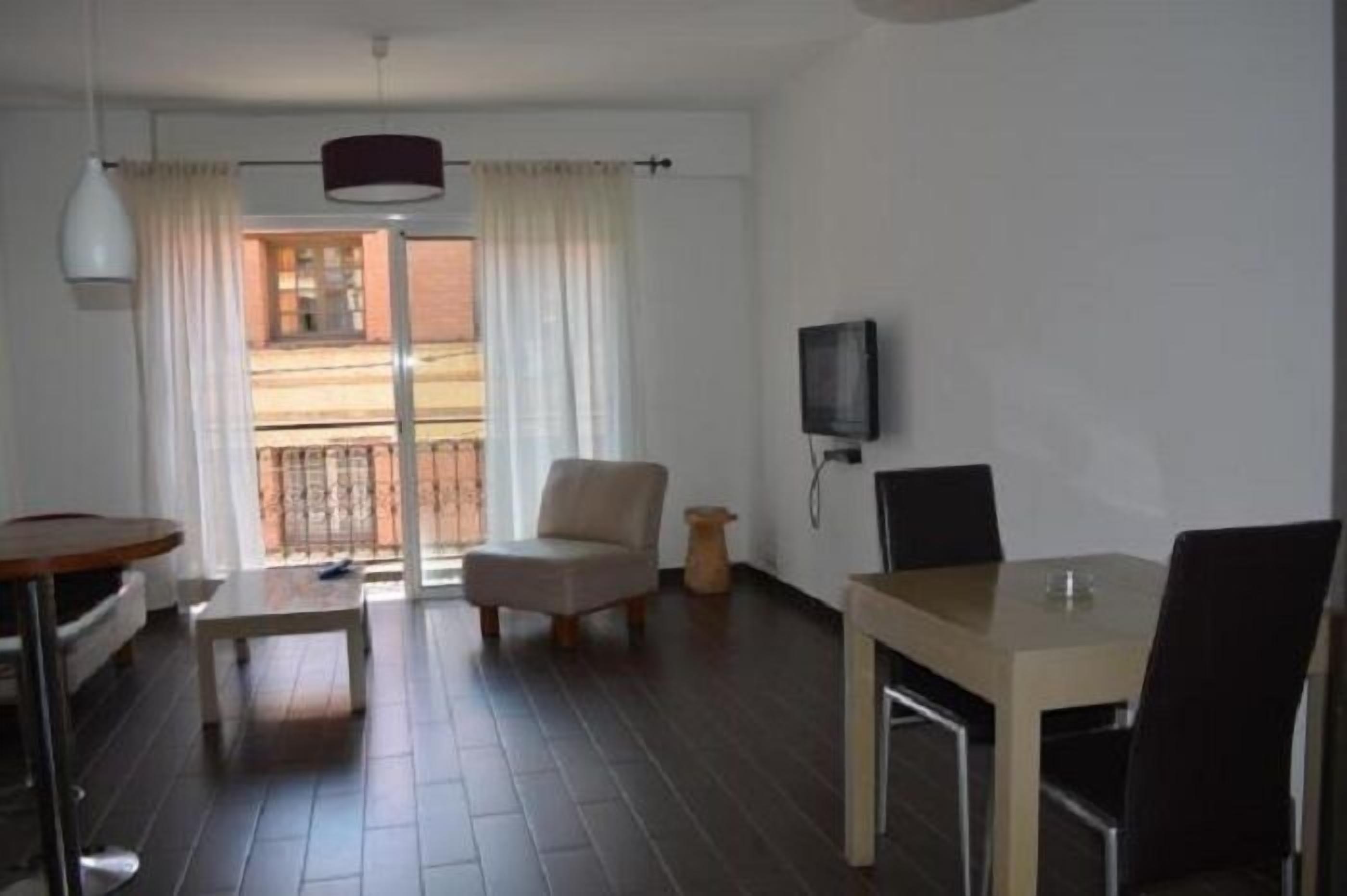 A modern living room with a sofa, a dining table, and a TV mounted on the wall.