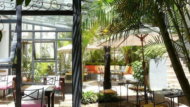 An indoor garden with tables and chairs, surrounded by lush greenery and a glass structure. - La Ribaudière (Antananarivo)