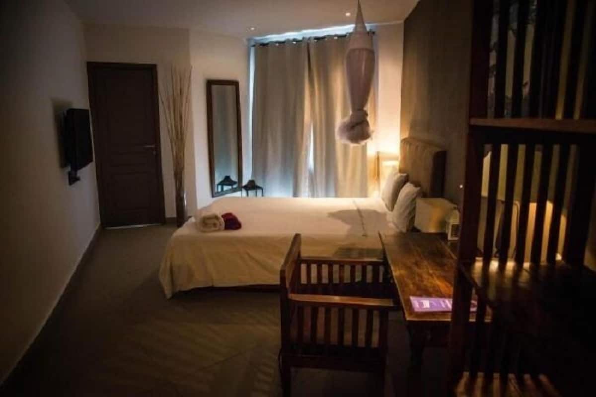 A hotel room with a bed, a wooden chair, a table, a hanging light fixture, and a door.