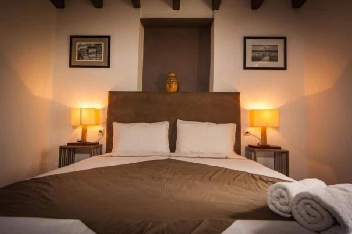 A neatly made bed with a brown headboard, two bedside lamps, and a rolled towel on the bed.