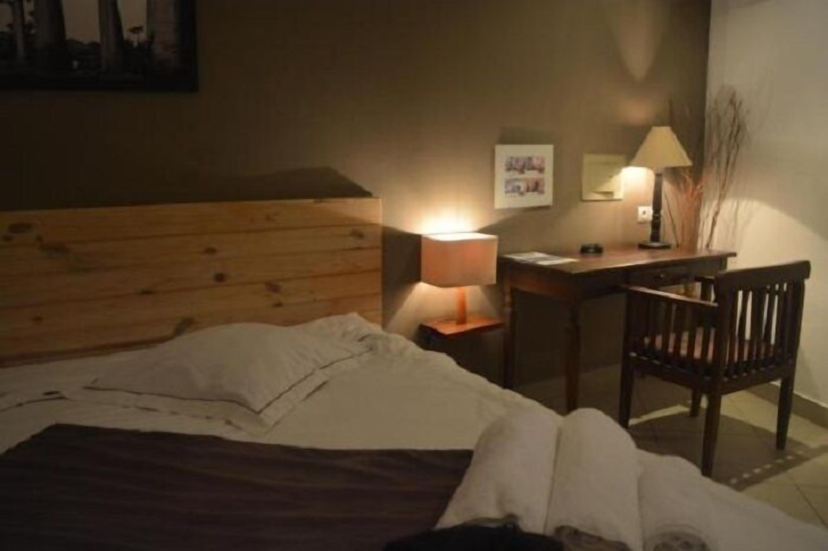Ein Hotelzimmer mit einem hölzernen Kopfende, einem Schreibtisch mit Lampe, einem Stuhl und einem Bett mit weißer Bettdecke.