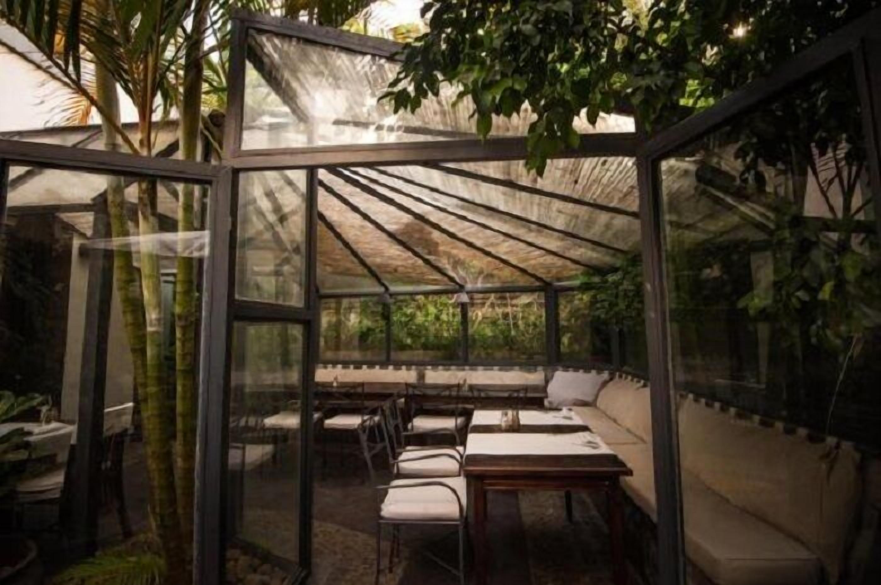 Een ruimte in kasstijl met tafels, stoelen, glazen wanden en planten.
