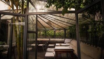 Een ruimte in kasstijl met tafels, stoelen, glazen wanden en planten.