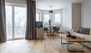 Relax in this serene living room with a large window offering a view of snow-covered trees, a comfortable sofa, and a dining area.