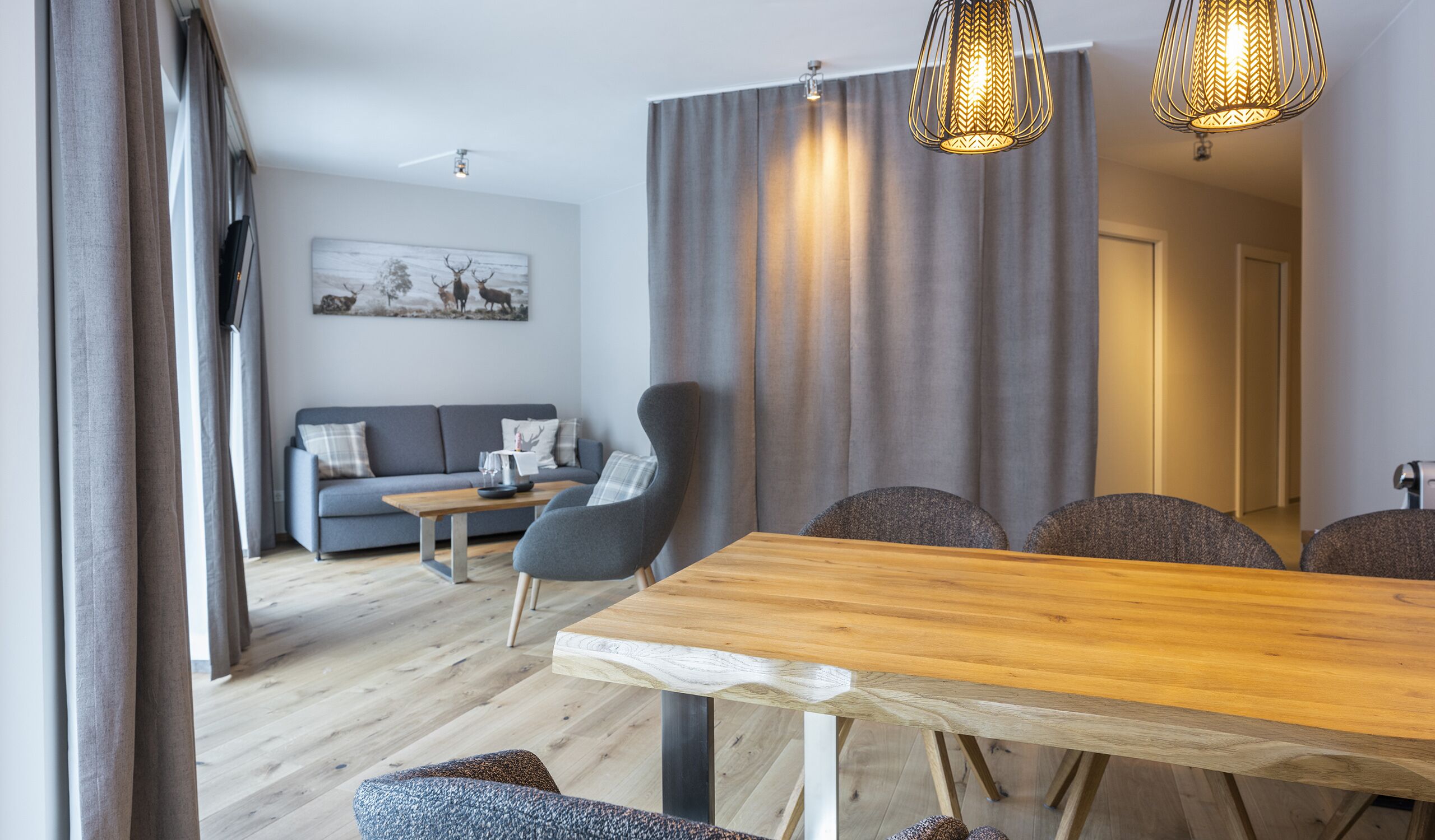 Un salon moderne avec une table à manger en bois, un canapé gris et un tableau accroché au mur.