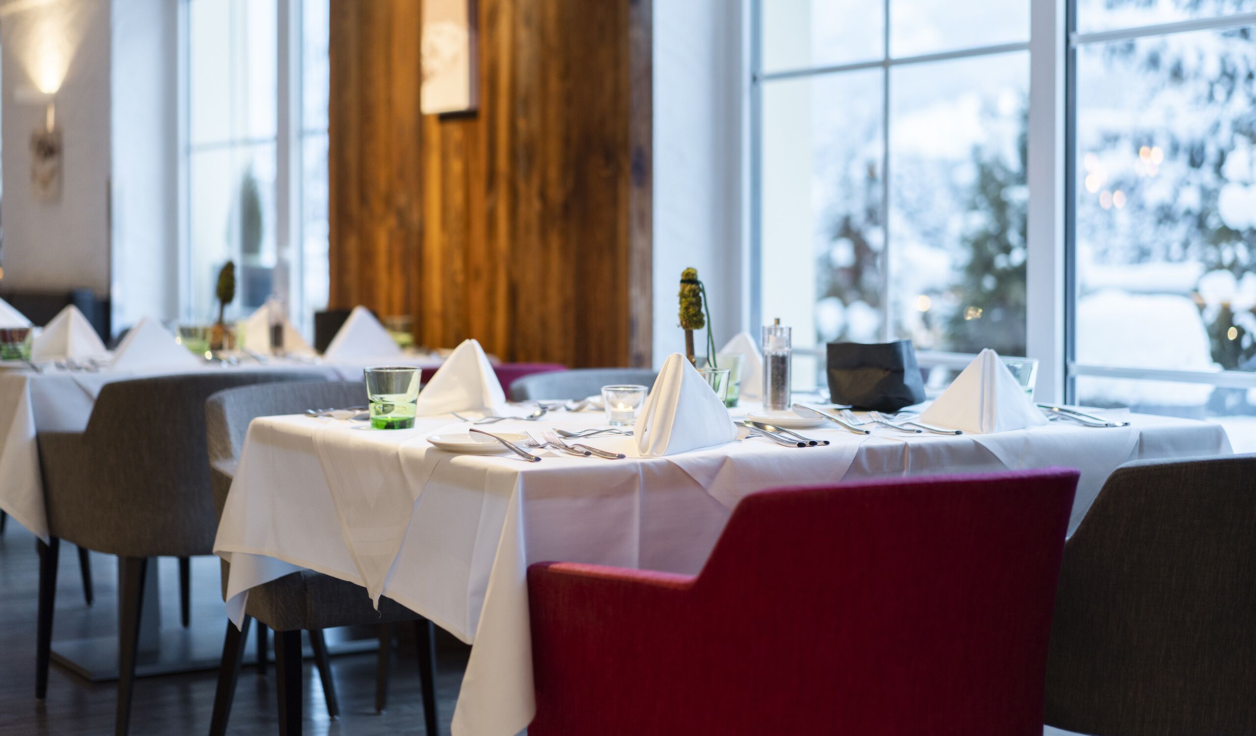 Ein Restaurant mit gedeckten Tischen und einer Aussicht auf eine verschneite Landschaft durch große Fenster.