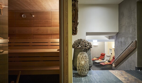A spa area with wooden benches, a large woven basket, and a staircase leading to a lounge with red chairs.