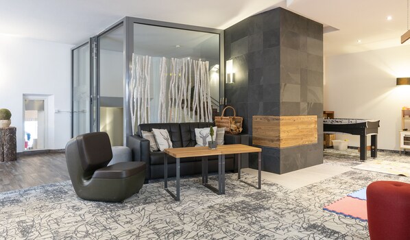 A modern living room with a glass partition, a sofa, a coffee table, and a foosball table. - Residenz Hochalm (Saalbach-Hinterglemm)