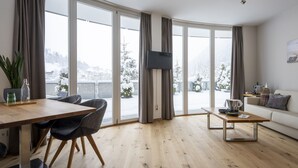 Una sala de estar moderna con piso de madera, un comedor con mesa y sillas, un sofá y un televisor montado en la pared.
