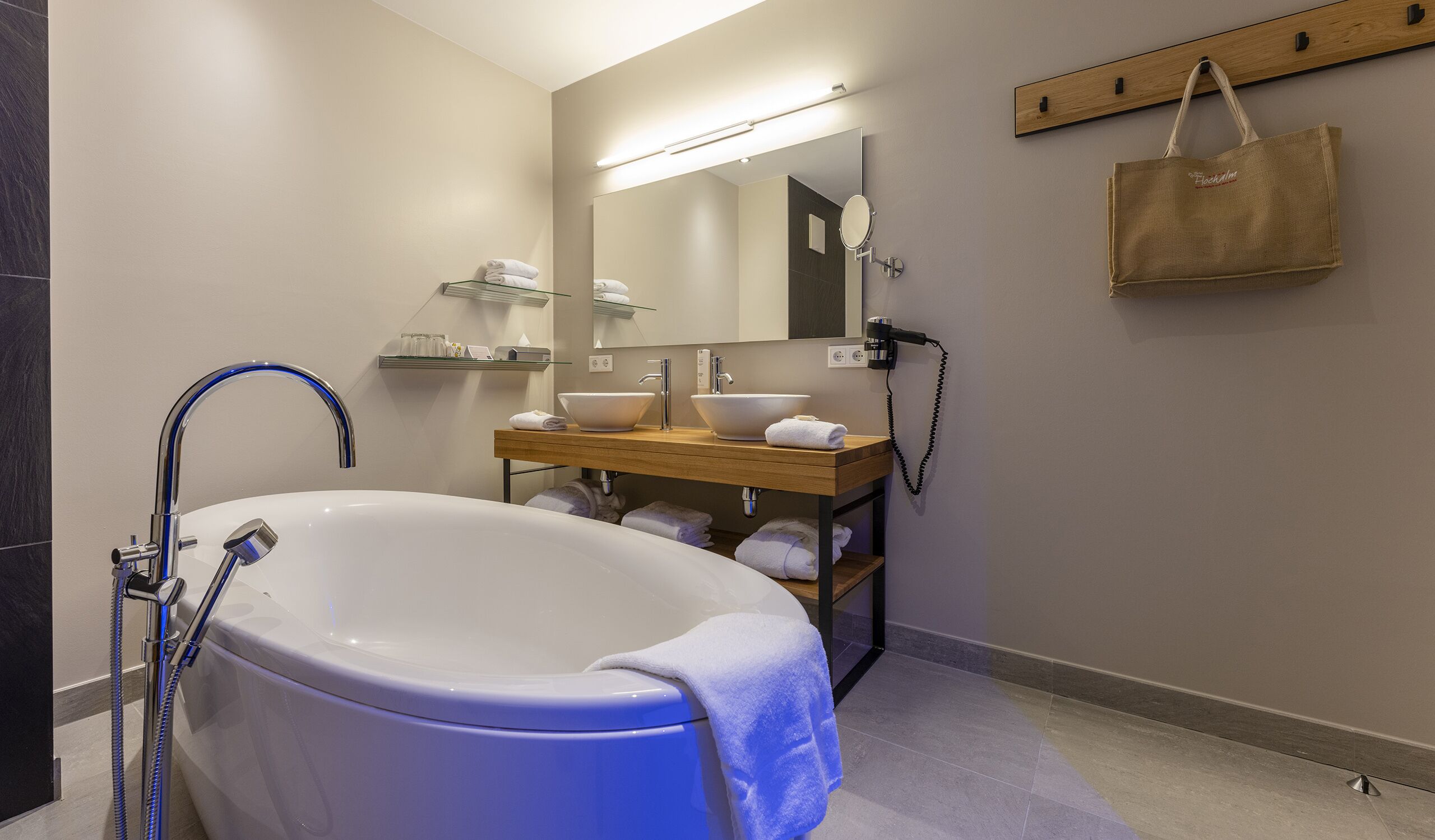 A modern bathroom with a freestanding bathtub, a wooden vanity with two sinks, a towel rack, and a mirror.