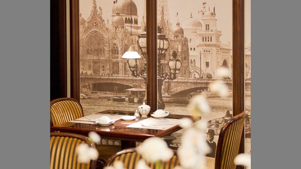 A dining area with a table set for two, a view of a historic building with a bridge, and a lamp on the table. - Gildors Hotel Atmosphère (Düsseldorf)