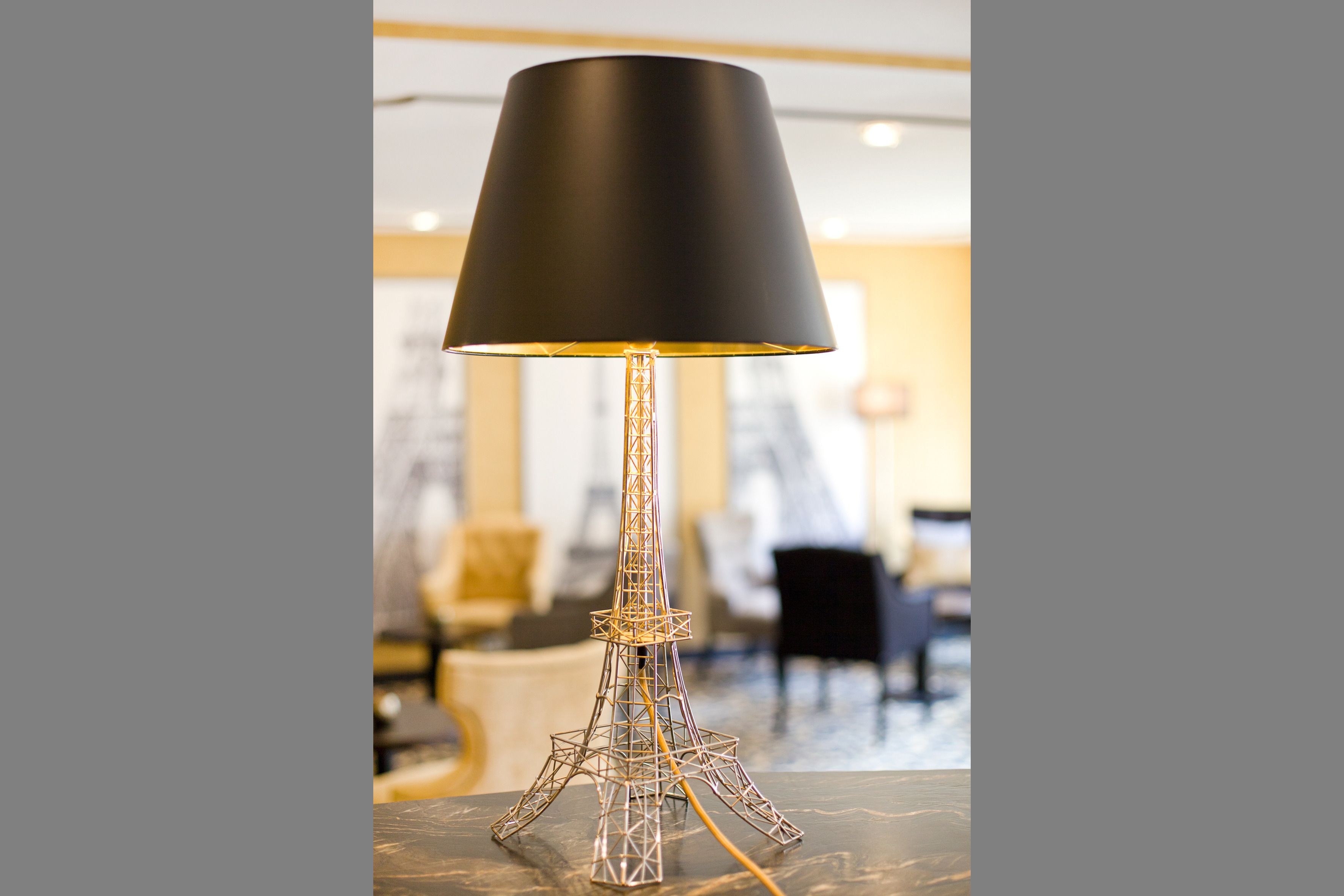 Una lámpara con pantalla negra y base de metal con forma de Torre Eiffel.