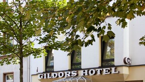 The exterior of the Gildors Hotel with a prominent sign, a large window, and a tree in the foreground. - Gildors Hotel Atmosphère (Düsseldorf)