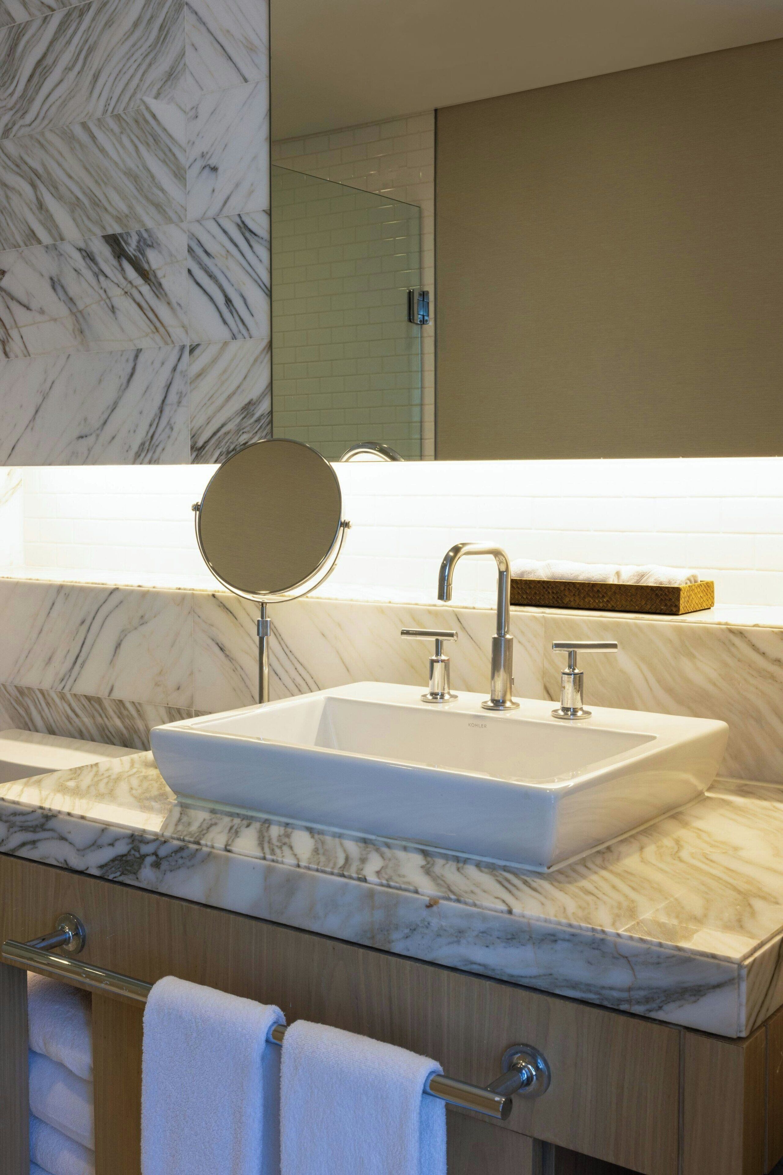 A modern bathroom with a marble sink, a round mirror, and a towel rack.