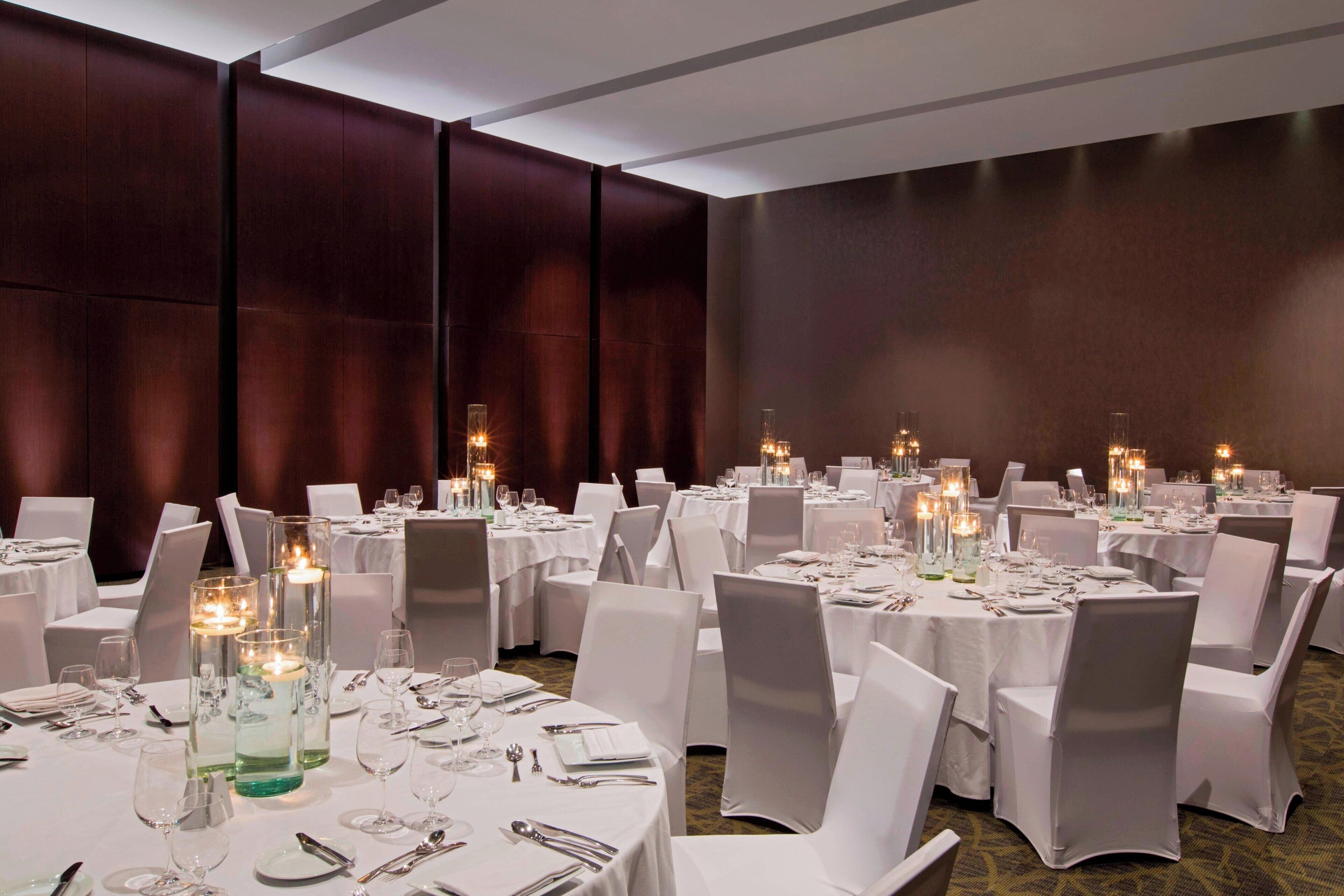 Een feestzaal met ronde tafels gedekt voor een diner, elk met witte tafelkleden en kandelaars.