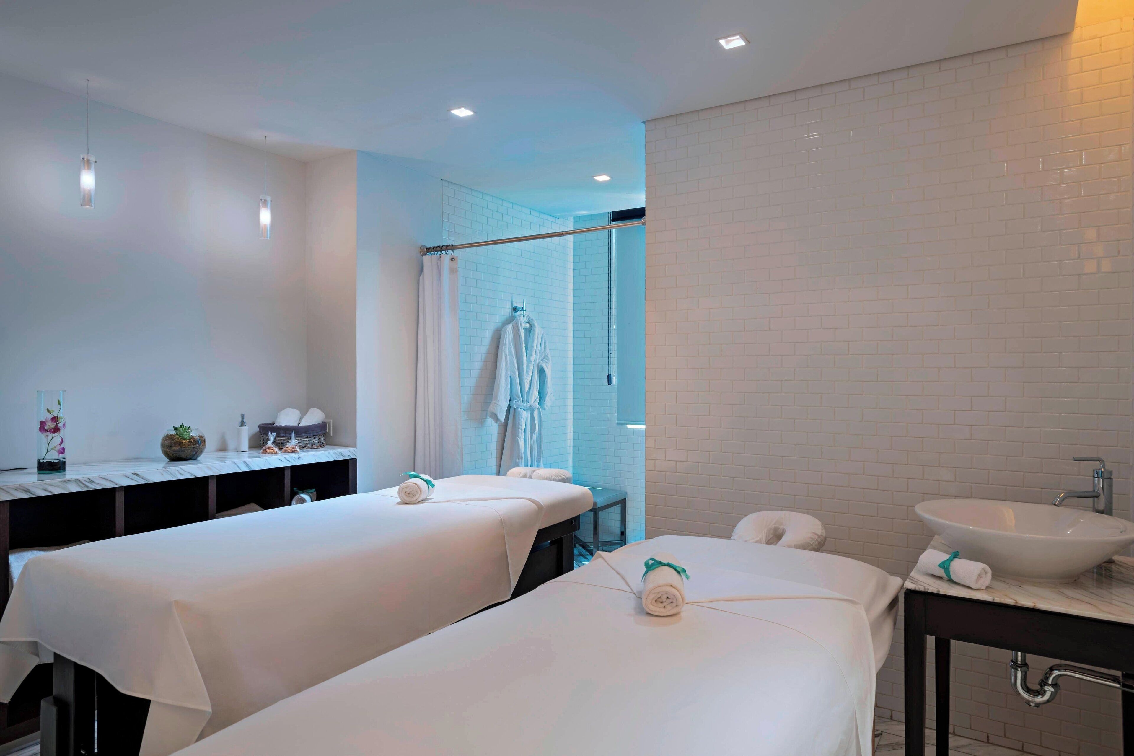 A modern bathroom with two massage tables, a sink, and a shower area.