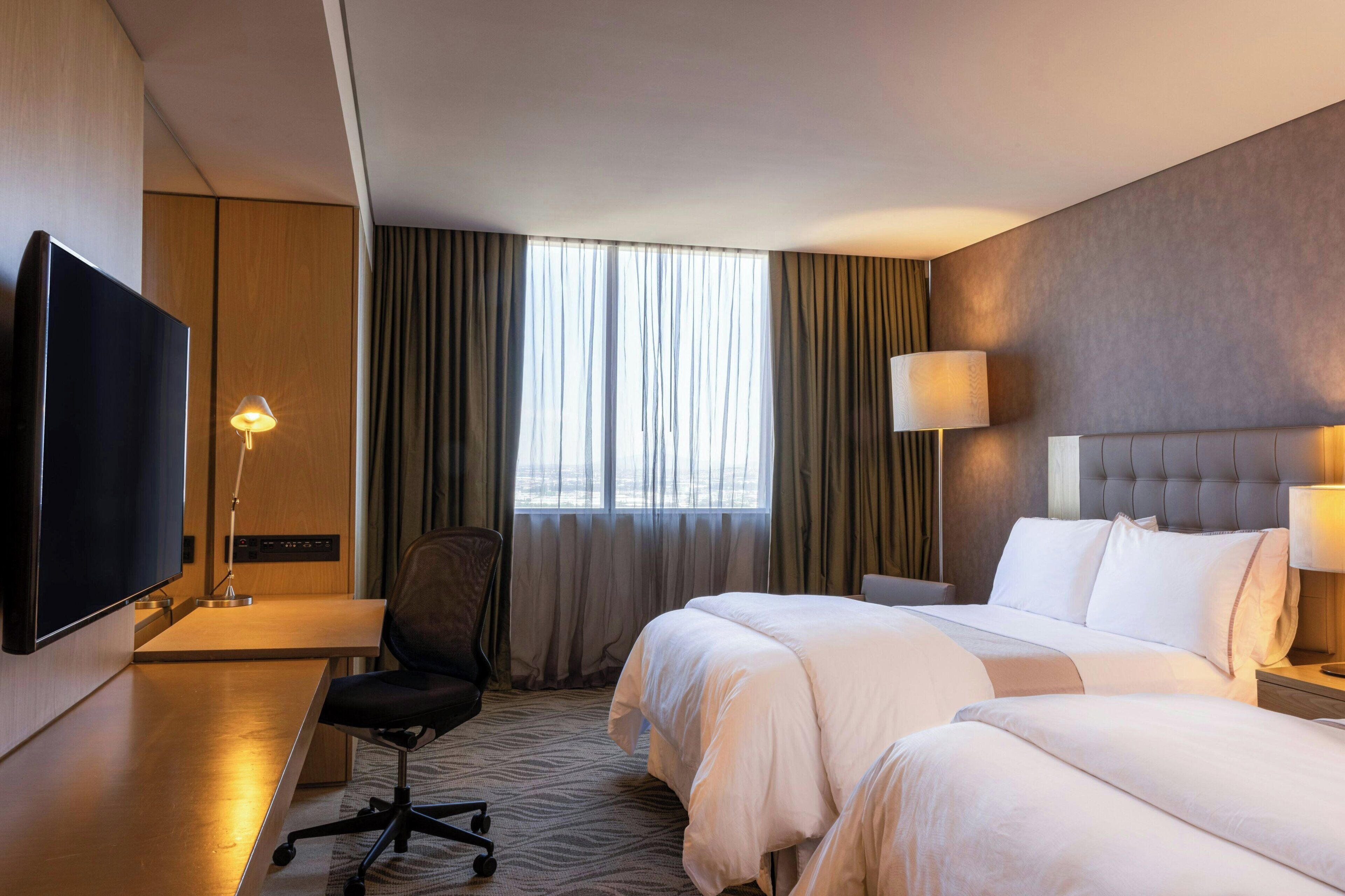 A hotel room with a large bed, a desk with a TV, and a chair.