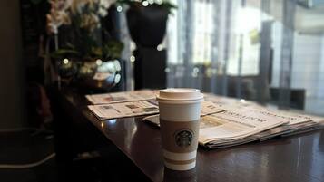 Une tasse de Starbucks sur une table en bois, avec des journaux et un vase de fleurs.