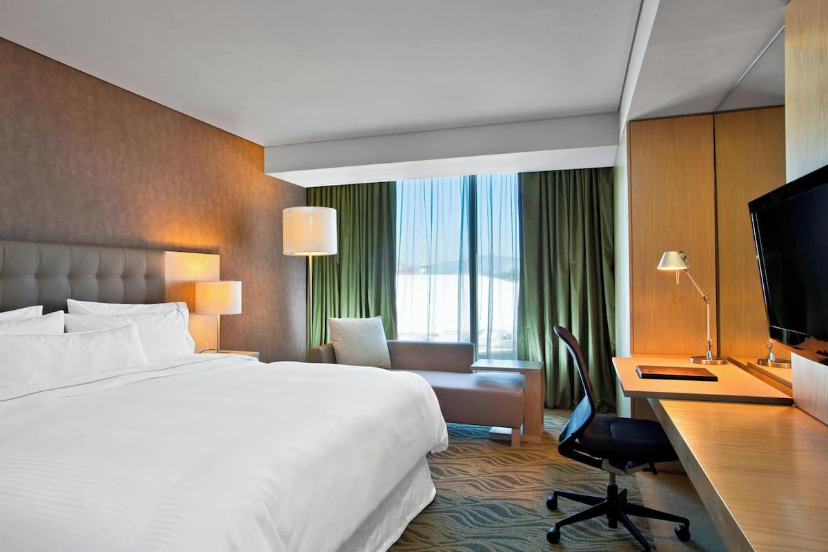 Ein Hotelzimmer mit einem großen Bett, einem Schreibtisch mit Computer, einem Sessel und einem Fernseher.