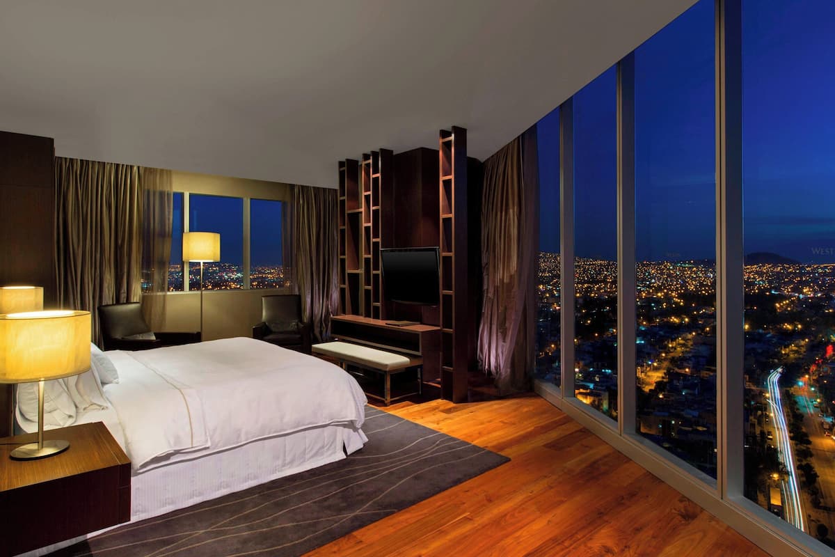Ein modernes Hotelzimmer mit einem großen Bett, einem Schreibtisch, einem Fernseher und Blick auf die Stadt.