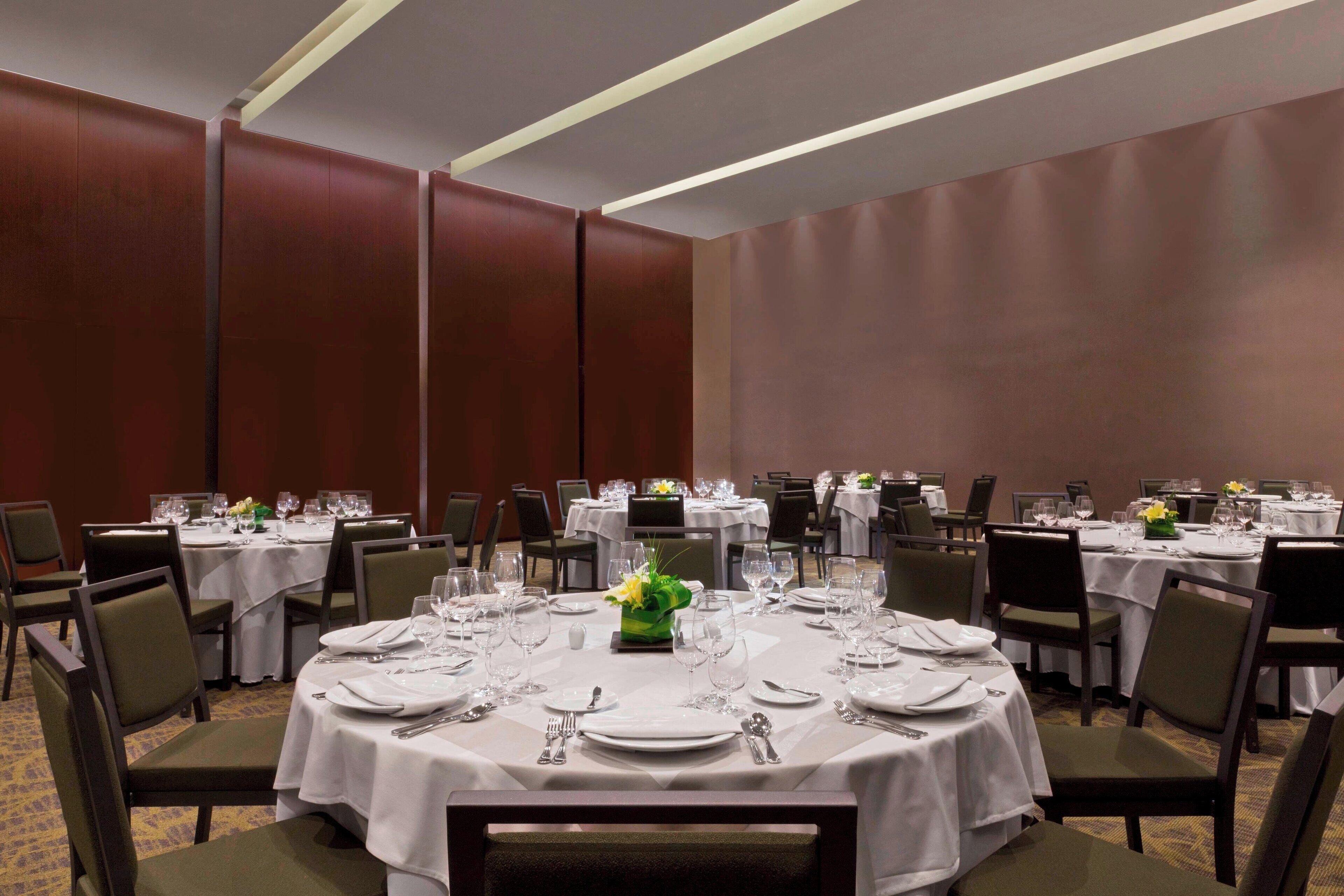 Une salle de conférence avec des tables rondes disposées pour un repas, agrémentée de nappes blanches, de chaises et de couverts.