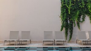 Uma área à beira da piscina com quatro espreguiçadeiras dispostas contra uma parede coberta de hera.