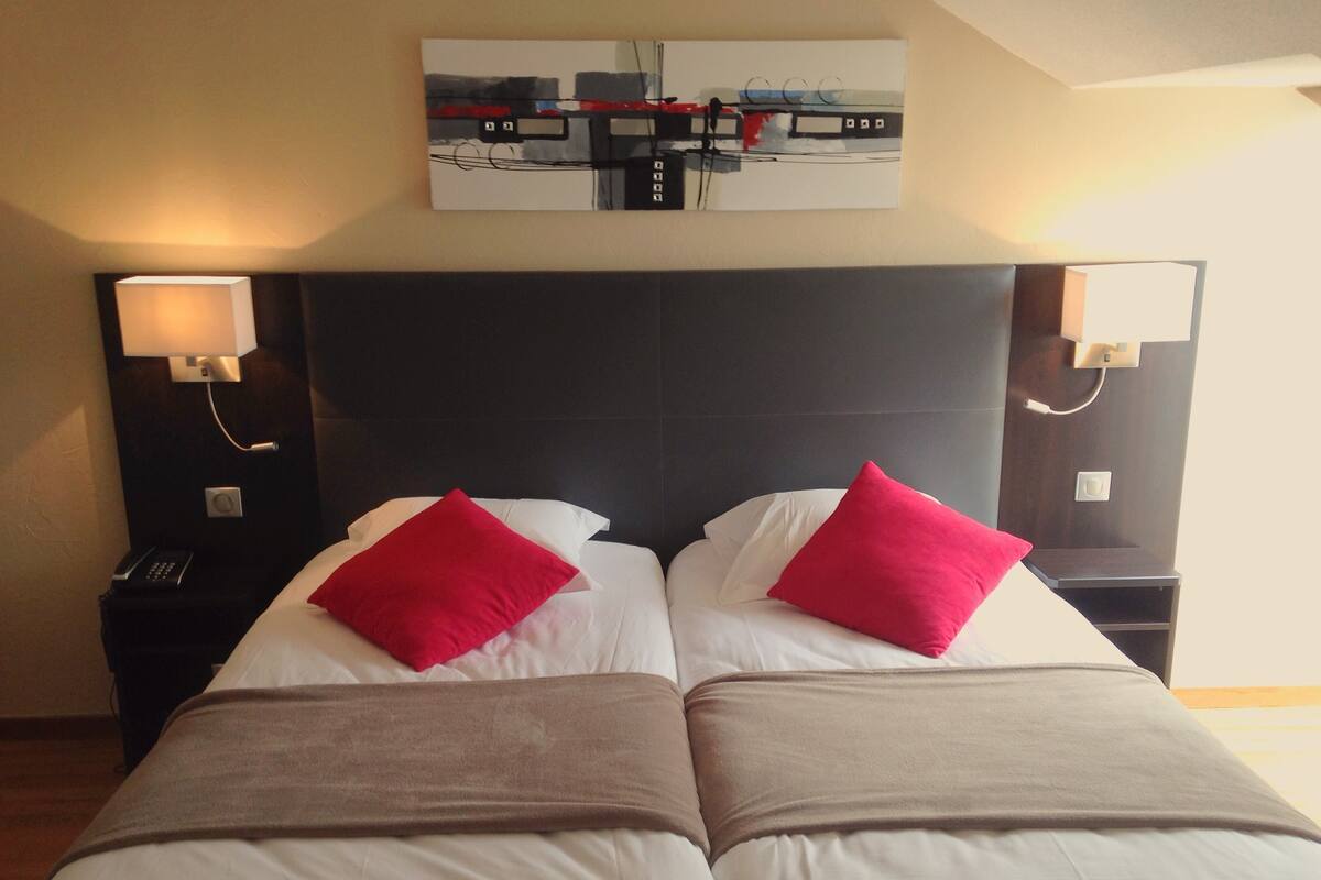Een tweepersoonsbed met twee rode kussens, een donker hoofdbord en een schilderij erboven.