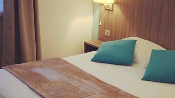 A hotel room with a bed, two pillows, a nightstand, a lamp, and a window with curtains.