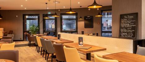 Un interior de restaurante con mesas y sillas de madera, iluminación colgante y un menú en la pizarra.