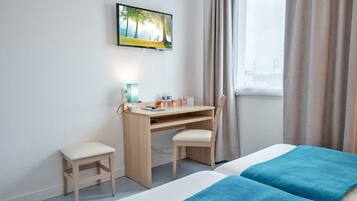 A hotel room with a bed, a desk with a chair, a TV mounted on the wall, and a window with curtains.
