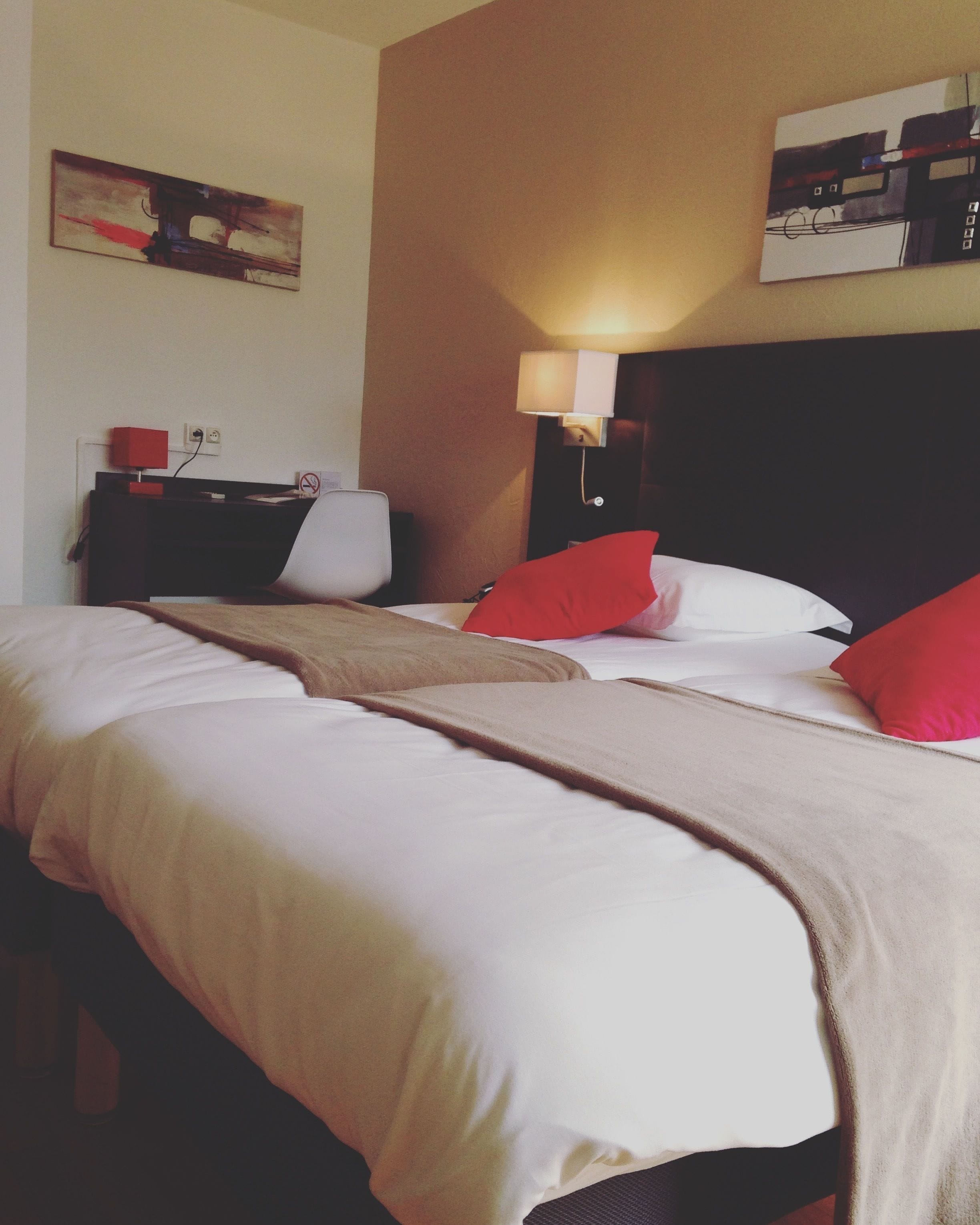 A hotel room with two beds, a nightstand, a lamp, and artwork on the walls.