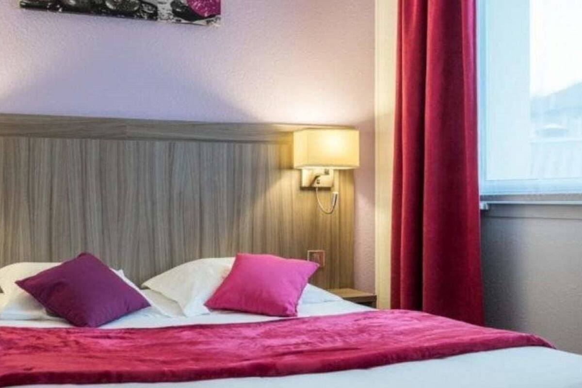 Een hotelkamer met een houten hoofdeinde, twee bedlampen, een bed met wit en roze beddengoed, en een rood gordijn.