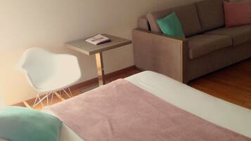 A bedroom with a bed, a white chair, a small table, and a sofa.