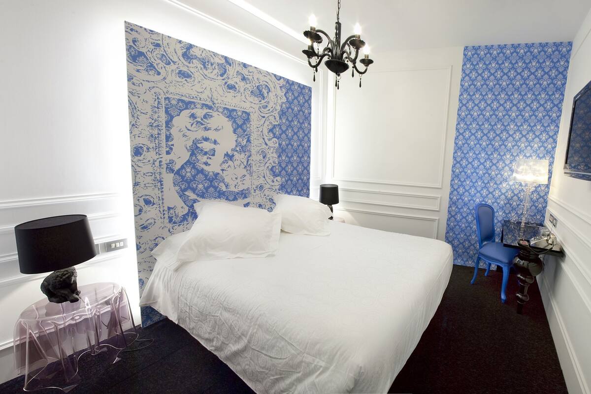 Ein Hotelzimmer mit Bett, Schreibtisch mit Stuhl, einer Kandelaber und Wandtapete mit Muster.