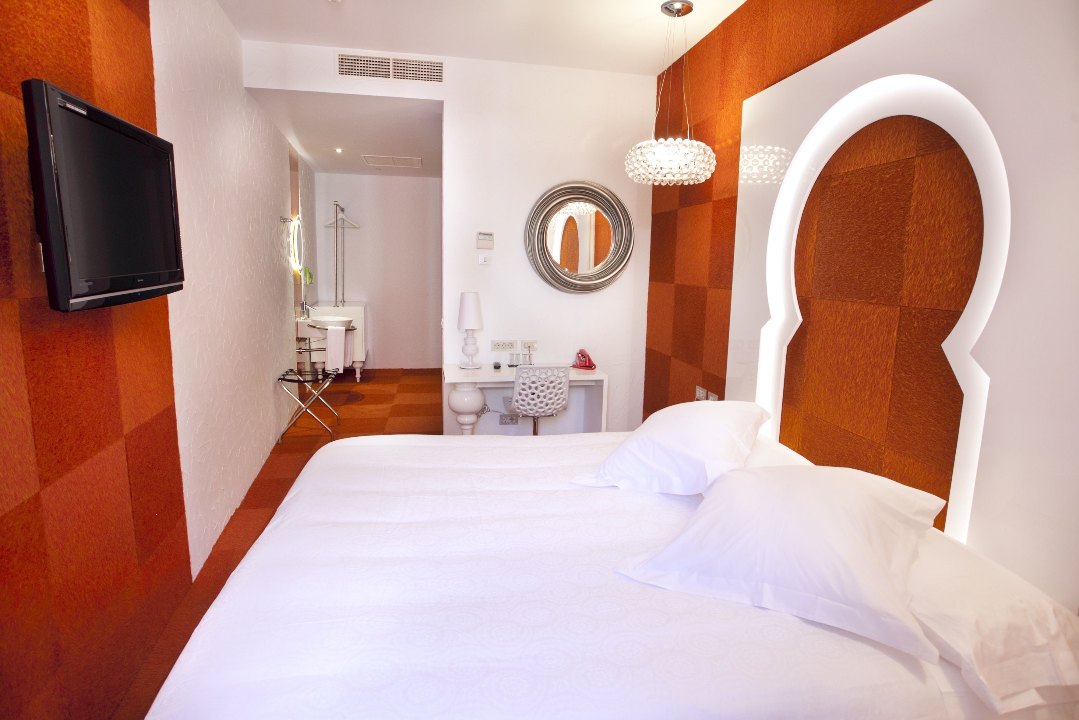 Camera d'albergo con un letto grande, una TV fissata al muro, uno specchio e un tavolino con una sedia.