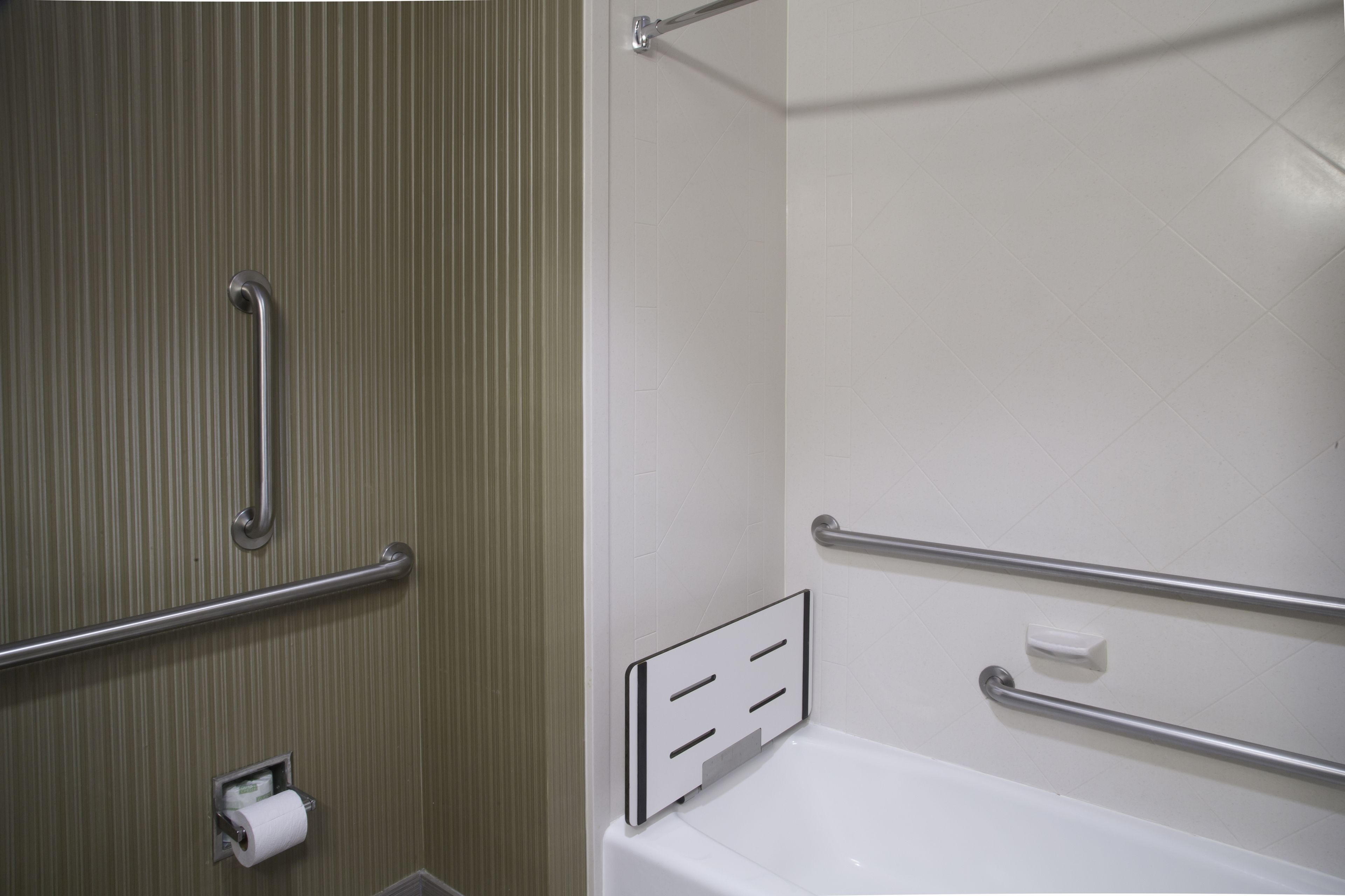 Un baño con inodoro, barras de apoyo y una bañera blanca.