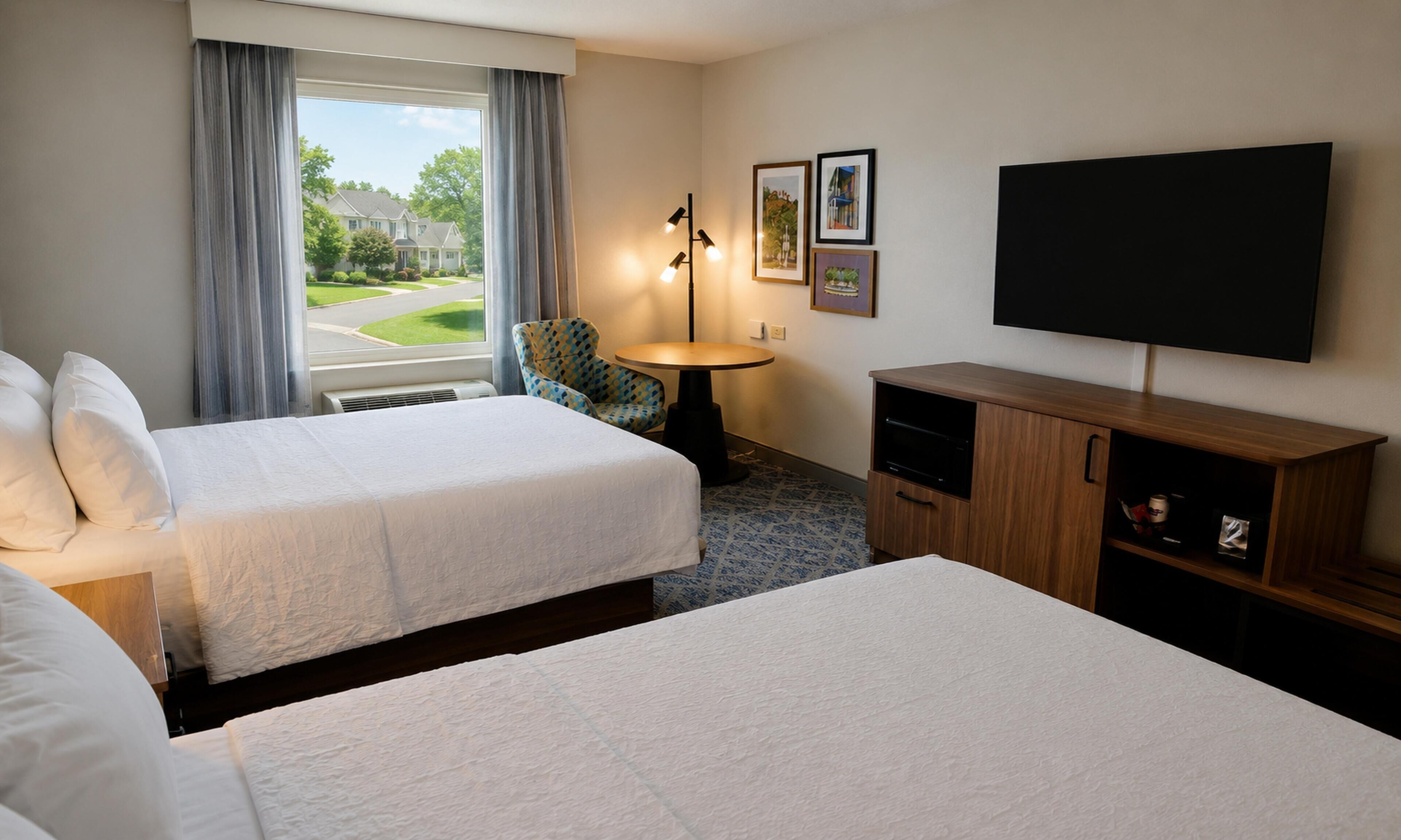 A hotel room with two beds, a TV, a small table, and a chair.