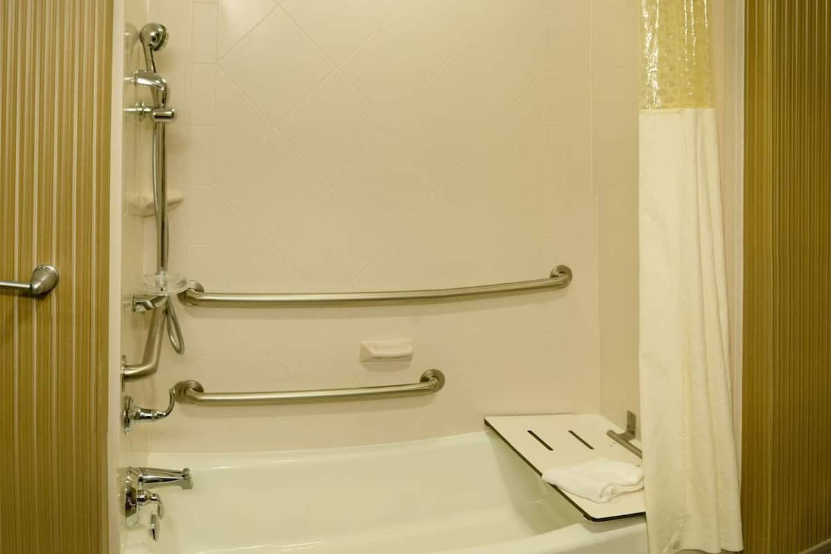 A standard hotel bathroom with a bathtub, shower, and handrails.